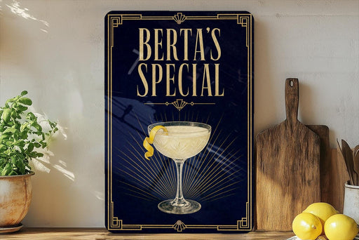 A framed poster with the text "BERTA'S SPECIAL" and an illustration of a cocktail glass with a lemon twist, placed on a wooden shelf next to a cutting board and a potted plant.