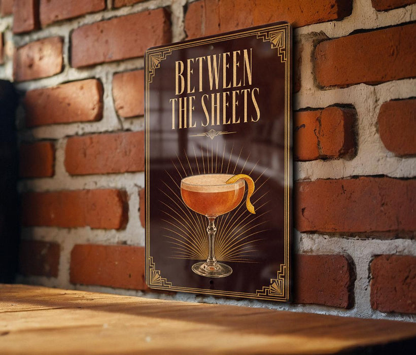 A sign with the text "BETWEEN THE SHEETS" and an illustration of a cocktail glass with a lemon peel.