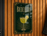A sign for "Bicyclette" cocktail, featuring a glass of yellow liquid with a lemon slice, is displayed on a wooden wall.