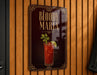 A sign for "Bloody Maria" cocktail, featuring a red drink with a garnish and a lime wedge, is displayed on a wooden wall.