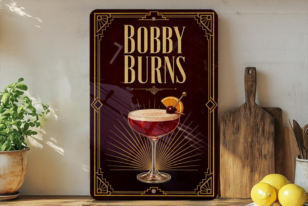 A decorative sign for "Bobby Burns" cocktail, featuring an illustration of a cocktail glass with a cherry on top, placed on a wooden surface next to a cutting board and some lemons.