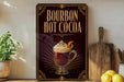 A decorative metal sign advertising "Bourbon Hot Cocoa" is displayed on a wooden shelf, accompanied by a potted plant, a wooden cutting board, and a bowl of lemons.