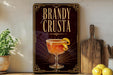 A framed advertisement for a Brandy Crusta cocktail, featuring an illustration of a glass with a lemon twist on the front.