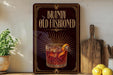 A framed advertisement for Brandy Old Fashioned, featuring an illustration of a glass of the drink with a decorative design.