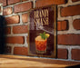 A framed illustration of a cocktail with a garnish, displayed on a brick wall.