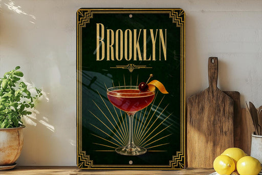 A decorative sign for "Brooklyn" featuring a cocktail glass with a cherry and lemon slice, placed on a wooden surface next to a cutting board and a potted plant.