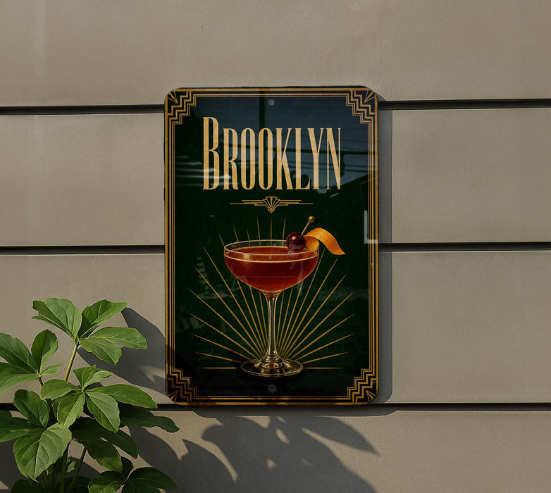 A decorative sign for "Brooklyn" featuring a cocktail glass with a cherry on top, placed on a wall next to a plant.