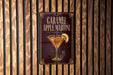 A sign for a caramel apple martini is displayed on a wooden wall.
