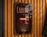 A decorative sign for "Cardinale" cocktail, featuring a glass of red wine with a lemon twist, is displayed on a wooden wall.