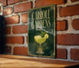 A sign for Carroll Gardens, featuring a cocktail glass with a lime garnish, is displayed on a brick wall.