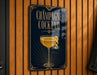 A sign for a champagne cocktail is displayed on a wooden wall.
