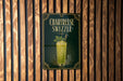 A poster advertising a "Chartreuse Swizzle" is displayed on a wooden wall.