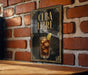 A sign with the text "CUBA LIBRE" and an illustration of a drink with ice cubes, placed on a wooden surface against a brick wall.