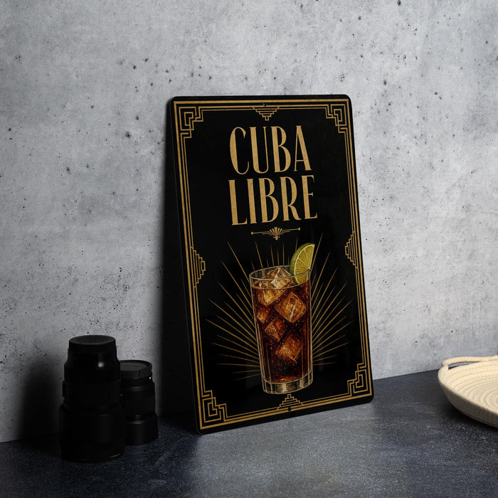 a framed poster with an illustration of a cocktail and the text "CUBA LIBRE" on it, placed on a countertop next to some black camera lenses.