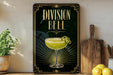 a framed advertisement for a cocktail called "Division Bell", which is displayed on a wall next to a wooden cutting board and some lemons.