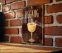 A decorative sign for "Eggnog" hangs on a brick wall, featuring an illustration of a glass filled with eggnog and a cinnamon stick.