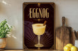 A framed poster of a glass of eggnog is displayed on a shelf, with a wooden cutting board and a potted plant to the side.