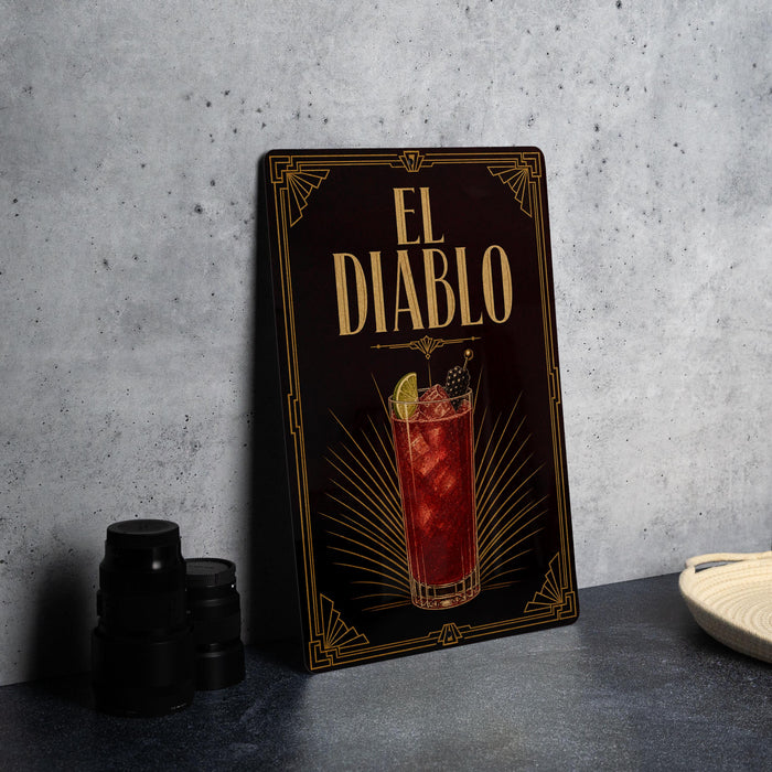 a decorative sign for "El Diablo", which is a cocktail, placed on a table next to some black camera lenses.