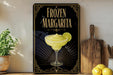 A framed poster of a frozen margarita is displayed on a wall, with a wooden cutting board and a potted plant to the side.