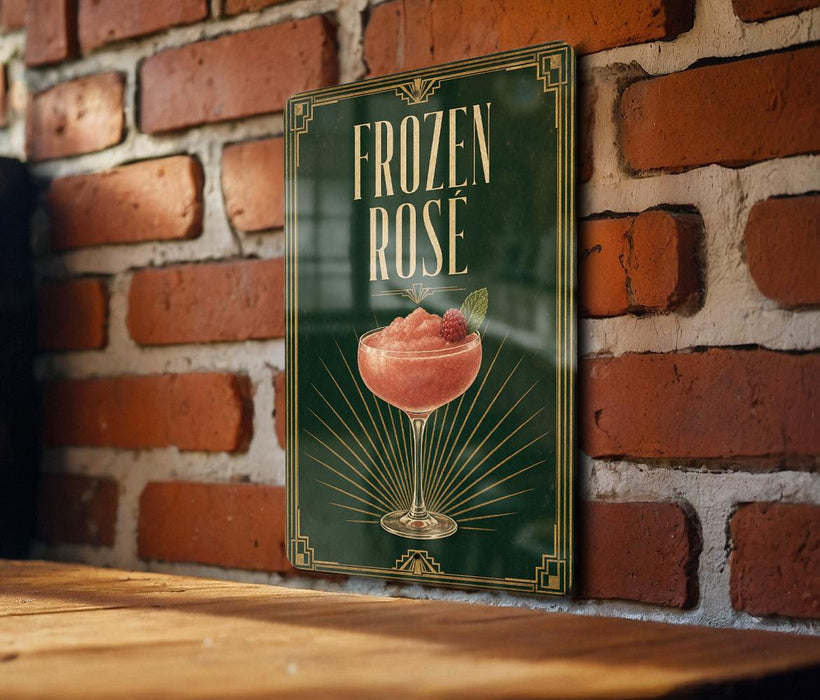 A framed poster with the title "FROZEN ROSE" and an illustration of a pink drink in a glass, hanging on a brick wall.