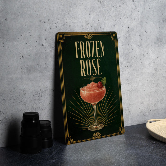A framed poster with the title "FROZEN ROSE" and an illustration of a pink drink in a glass, placed on a gray countertop next to a stack of black containers.