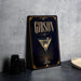 A framed poster of a martini glass with the word "GIBSON" on it, placed on a gray countertop next to some black camera lenses.