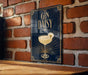 A decorative sign with the text "GIN DAISY" and an illustration of a cocktail glass with a flower on it, mounted on a brick wall.