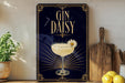 A decorative sign with the text "GIN DAISY" and an illustration of a cocktail glass with a flower on it, placed on a wooden surface next to a cutting board and some lemons.