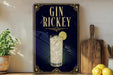 A framed advertisement for a gin and tonic drink, featuring a glass of the beverage with a lime slice and a decorative border.