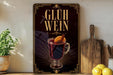 A framed poster with the text "GLÜH WEIN" and an illustration of a glass of red liquid, possibly a hot beverage, garnished with an orange slice.