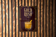 A poster with the text "GOLD RUSH" and an illustration of a cocktail is displayed on a wooden wall.