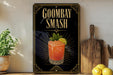 A black sign with gold trim displaying the text "GOOMBAY SMASH" and an illustration of a cocktail with a lemon slice.