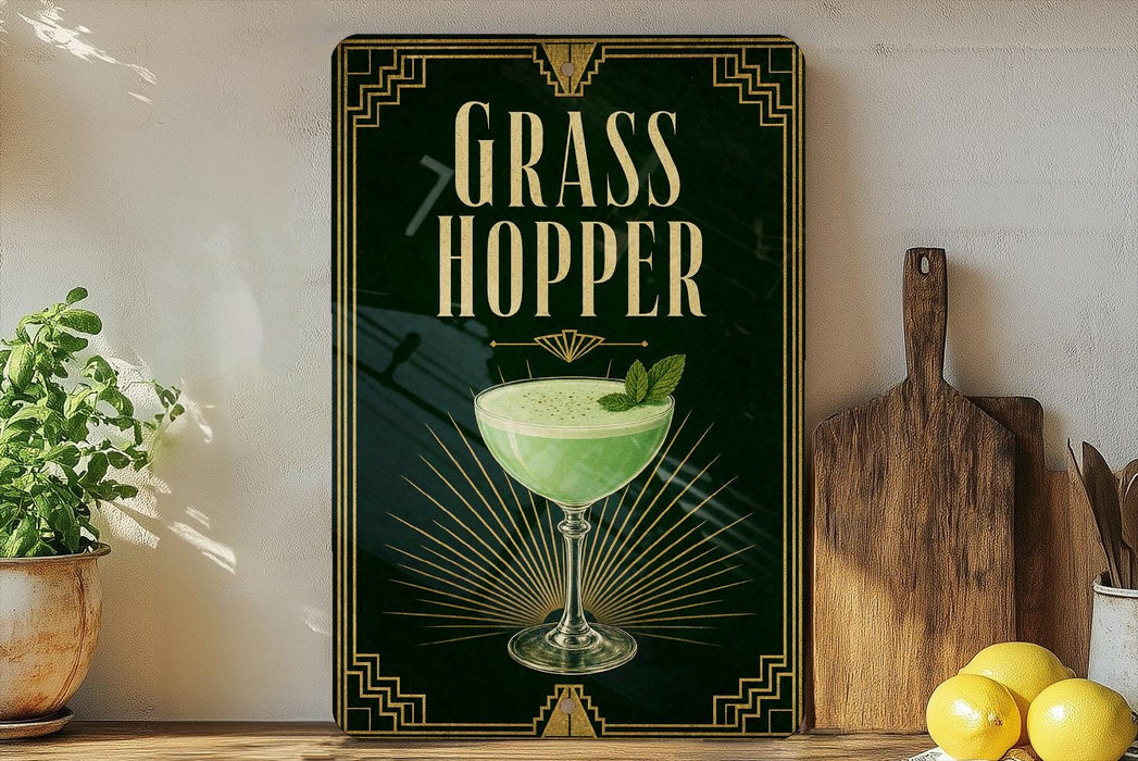 A framed poster with the title "GRASS HOPPER" displayed prominently, featuring an illustration of a green cocktail with a garnish. The poster is set against a dark background with a decorative border, and there are some potted plants and kitchen utensils visible in the foreground.
