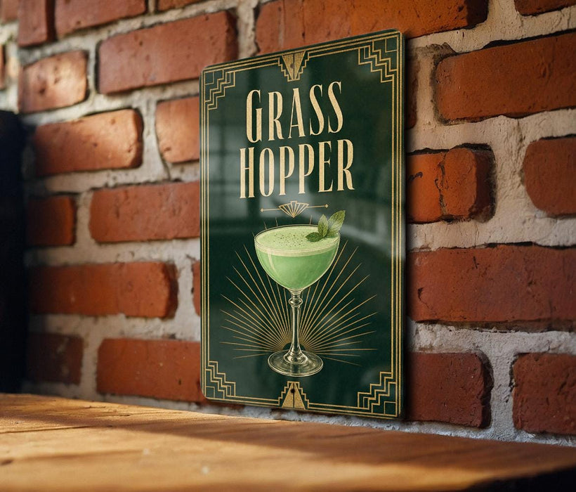 A sign with the text "GRASS HOPPER" and an illustration of a cocktail glass with a green drink in it, mounted on a brick wall.