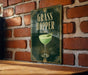 A sign with the text "GRASS HOPPER" and an illustration of a cocktail glass with a green drink in it, mounted on a brick wall.