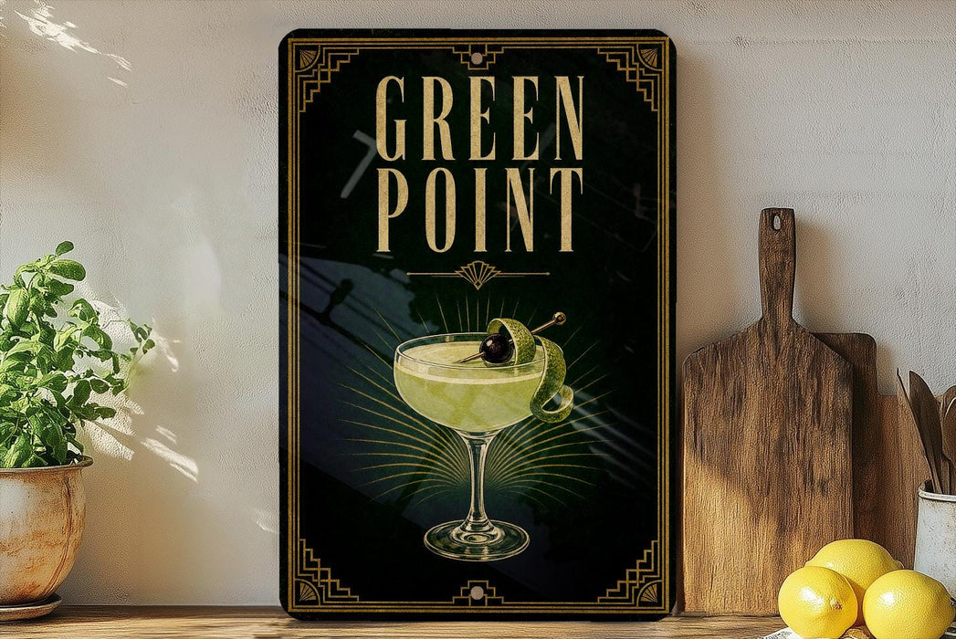 A framed poster with the text "GREEN POINT" and an illustration of a cocktail glass with a lemon slice on it, placed on a wooden shelf next to a wooden cutting board and a potted plant.