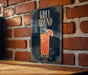A framed poster of a cocktail called "Greyhound" is displayed on a brick wall.