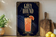 A framed advertisement for a cocktail called "Greyhound" featuring a glass of orange drink with a slice of lemon.