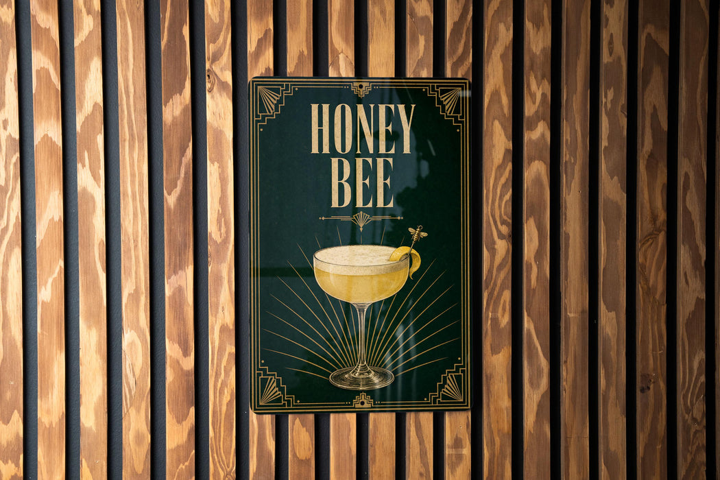 A poster with the text "HONEY BEE" and an illustration of a cocktail glass with a lemon slice, hanging on a wooden wall.