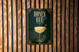 A poster with the text "HONEY BEE" and an illustration of a cocktail glass with a lemon slice, hanging on a wooden wall.