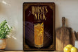 a decorative sign with the text "HORSE'S NECK" and an illustration of a glass of amber-colored liquid, possibly a cocktail or a mixed drink. The sign is displayed on a wooden surface, with a potted plant, a wooden cutting board, and some lemons nearby.