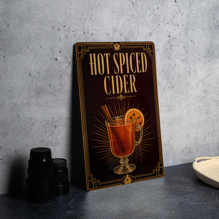 A sign advertising "Hot Spiced Cider" is displayed on a gray countertop, with a glass of the beverage and cinnamon sticks visible.