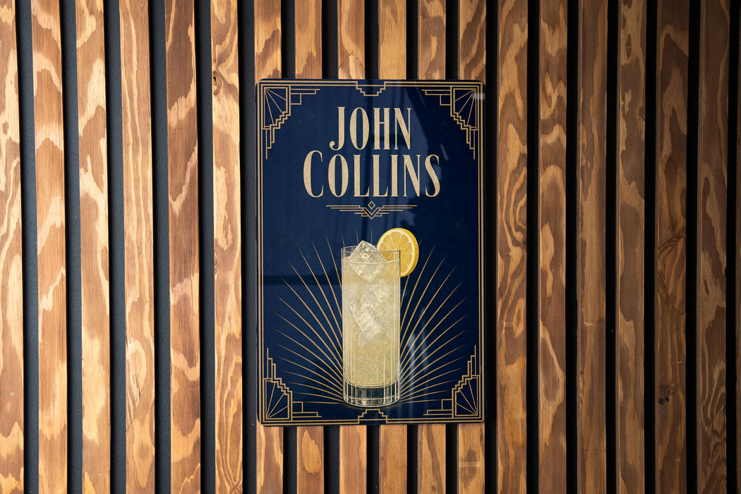 A poster for a cocktail called "John Collins" is displayed on a wooden wall.