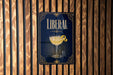 A metal sign with the word "LIBERAL" on it, featuring an illustration of a cocktail glass with a lemon peel.