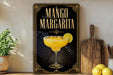A framed poster of a mango margarita cocktail is displayed on a wall, with a wooden cutting board and a potted plant to the side.