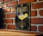 A framed poster of a margarita glass is displayed on a brick wall.