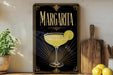 A framed poster of a margarita glass with a lime slice, placed on a shelf next to a wooden cutting board and a potted plant.