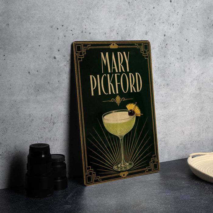A decorative sign for "Mary Pickford" cocktail, featuring an illustration of a cocktail glass with a cherry on top, is displayed on a table next to some black camera lenses.