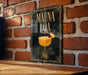 a sign with the text "MAUNA LOA" and an illustration of a cocktail glass with a cherry on top, set against a brick wall background.