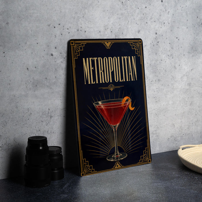A framed poster of a cocktail called "Metropolitan" is displayed on a wall, with a glass of red cocktail and a lemon on the poster.